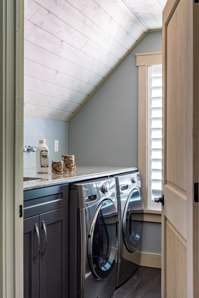 This is an example of a mid-sized country single-wall dedicated laundry room in Other with an undermount sink, shaker cabinets, black cabinets, grey walls, medium hardwood floors, a side-by-side washer and dryer, brown floor and beige benchtop.