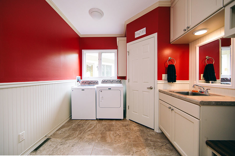 This is an example of a mid-sized transitional u-shaped utility room in Other with a single-bowl sink, recessed-panel cabinets, white cabinets, red walls, porcelain floors, a side-by-side washer and dryer, brown floor and beige benchtop.