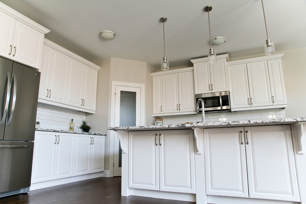 Eat-in kitchen - mid-sized transitional l-shaped dark wood floor and brown floor eat-in kitchen idea in Toronto with an undermount sink, raised-panel cabinets, white cabinets, granite countertops, white backsplash, subway tile backsplash, stainless steel appliances and an island