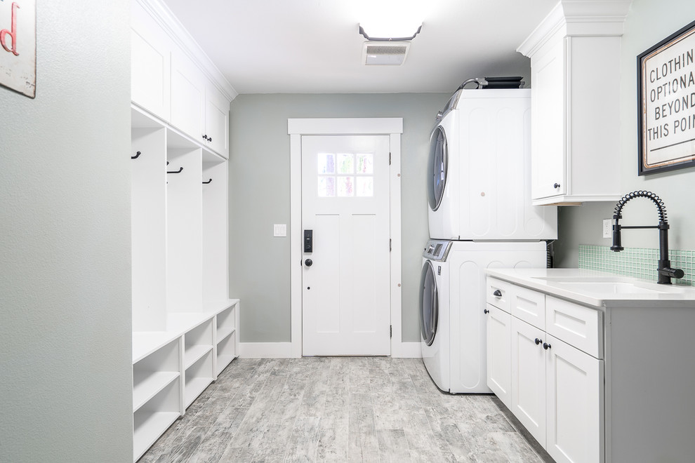 This is an example of a transitional galley laundry room in Seattle with an undermount sink, shaker cabinets, white cabinets, quartzite benchtops, grey walls, porcelain floors, a stacked washer and dryer, grey floor and white benchtop.