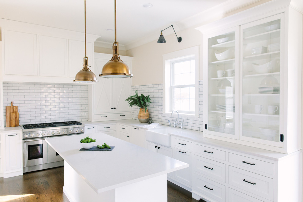 Inspiration for a mid-sized country l-shaped eat-in kitchen in Chicago with a farmhouse sink, shaker cabinets, white cabinets, quartz benchtops, white splashback, subway tile splashback, stainless steel appliances, medium hardwood floors and with island.