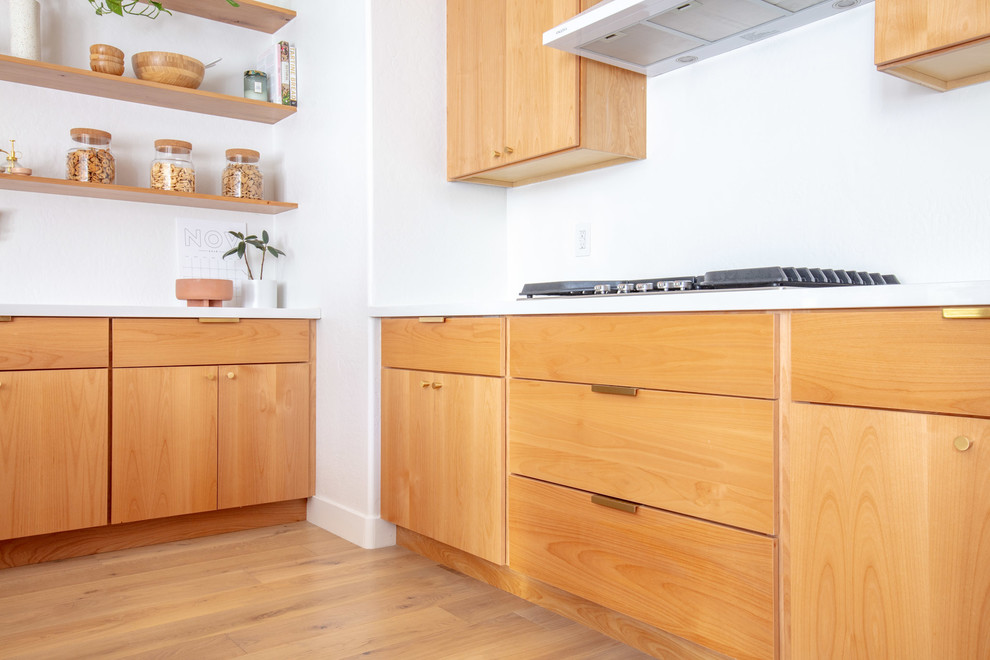 Mid-sized midcentury u-shaped eat-in kitchen in Phoenix with an undermount sink, flat-panel cabinets, light wood cabinets, quartz benchtops, white splashback, stainless steel appliances, light hardwood floors, with island, brown floor and white benchtop.