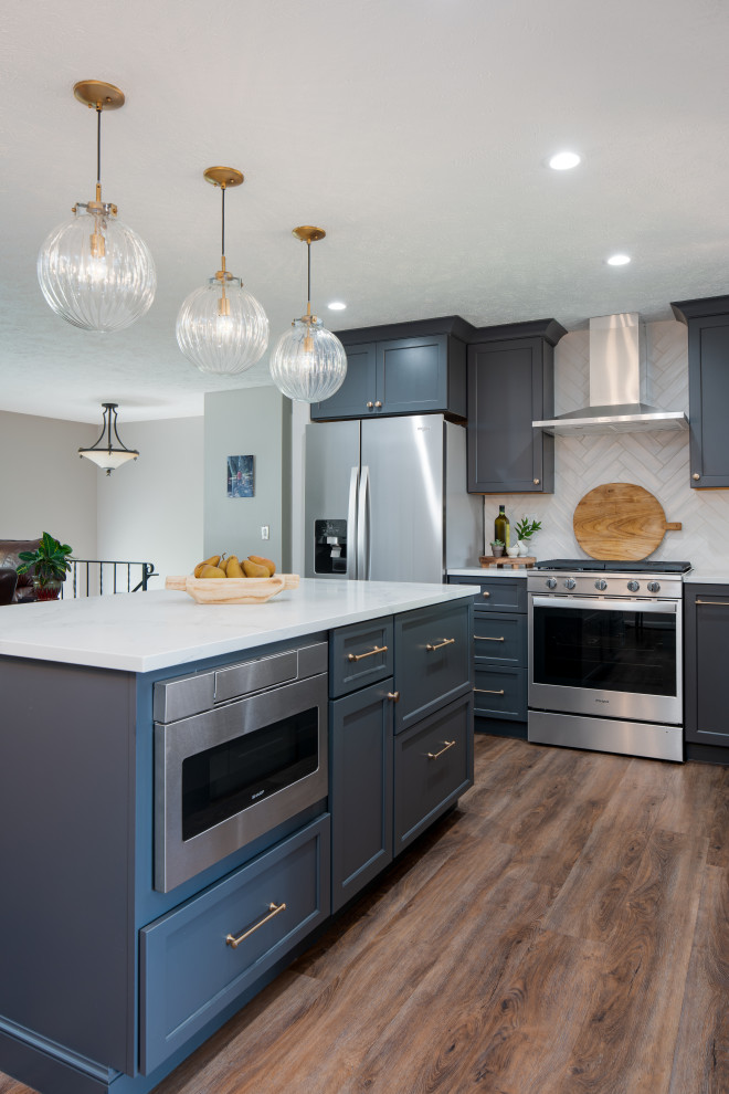 Photo of a mid-sized transitional u-shaped eat-in kitchen in Seattle with a drop-in sink, shaker cabinets, blue cabinets, solid surface benchtops, white splashback, porcelain splashback, stainless steel appliances, medium hardwood floors, with island, brown floor and white benchtop.