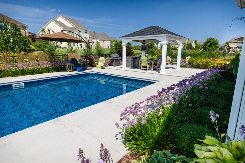 Design ideas for a mid-sized traditional backyard rectangular pool in Milwaukee with a water feature and concrete slab.
