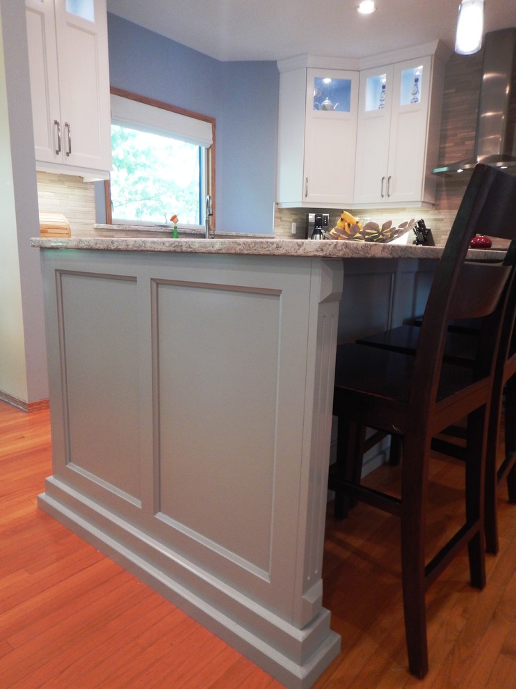 Example of a large transitional l-shaped light wood floor eat-in kitchen design with an undermount sink, recessed-panel cabinets, white cabinets, quartz countertops, gray backsplash, stone tile backsplash, stainless steel appliances and an island