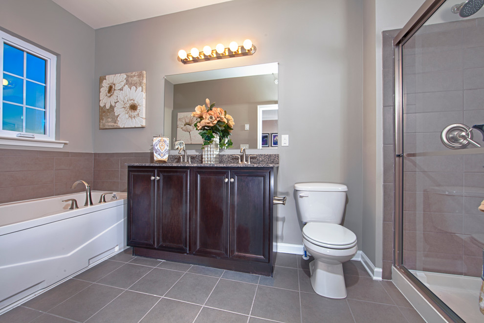 This is an example of a mid-sized contemporary master bathroom in Wilmington with an undermount sink, recessed-panel cabinets, dark wood cabinets, granite benchtops, a freestanding tub, an alcove shower, a one-piece toilet, gray tile, ceramic tile, grey walls and ceramic floors.