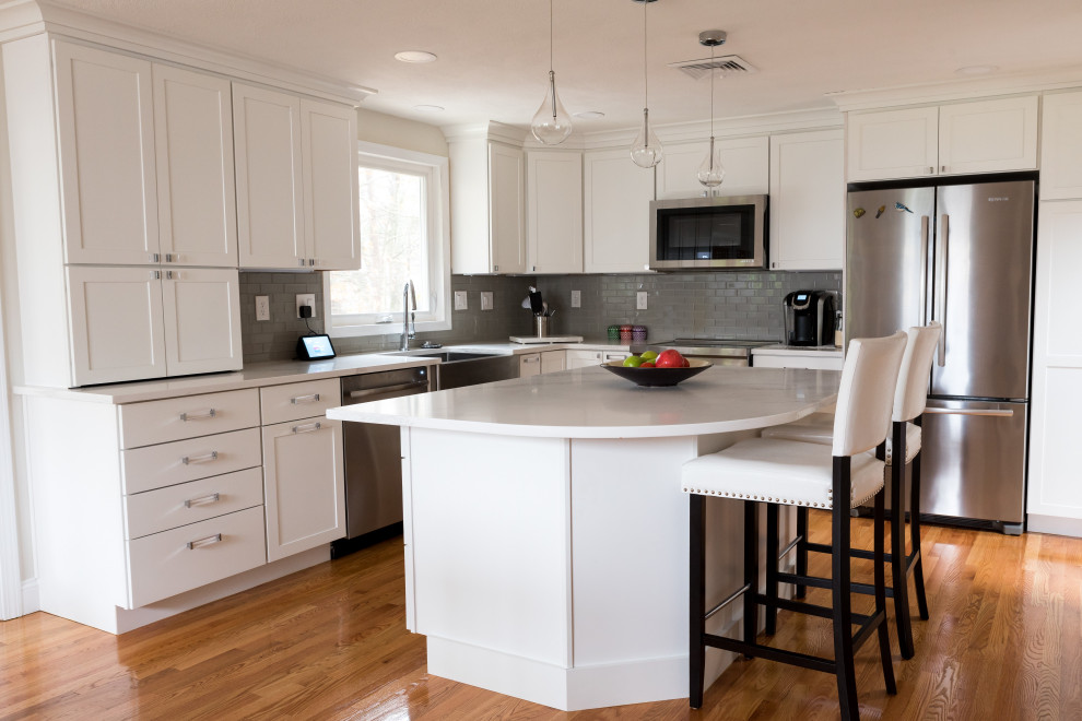 Eat-in kitchen - mid-sized transitional l-shaped light wood floor and brown floor eat-in kitchen idea in Boston with a farmhouse sink, shaker cabinets, white cabinets, quartz countertops, gray backsplash, ceramic backsplash, stainless steel appliances, an island and white countertops