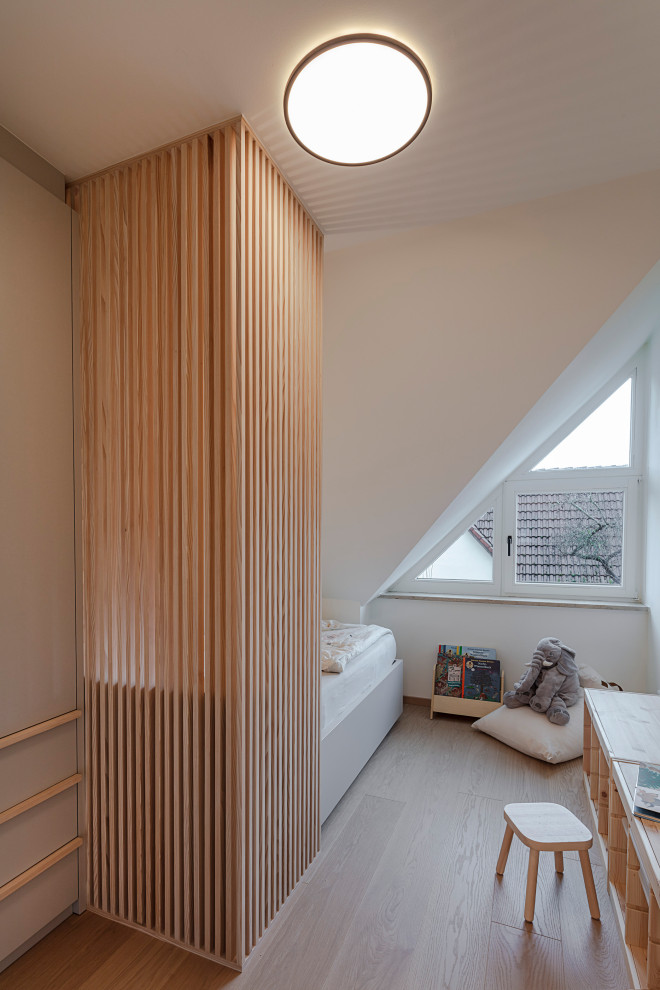 This is an example of a small scandi gender neutral toddler’s room in Munich with beige walls, light hardwood flooring and beige floors.