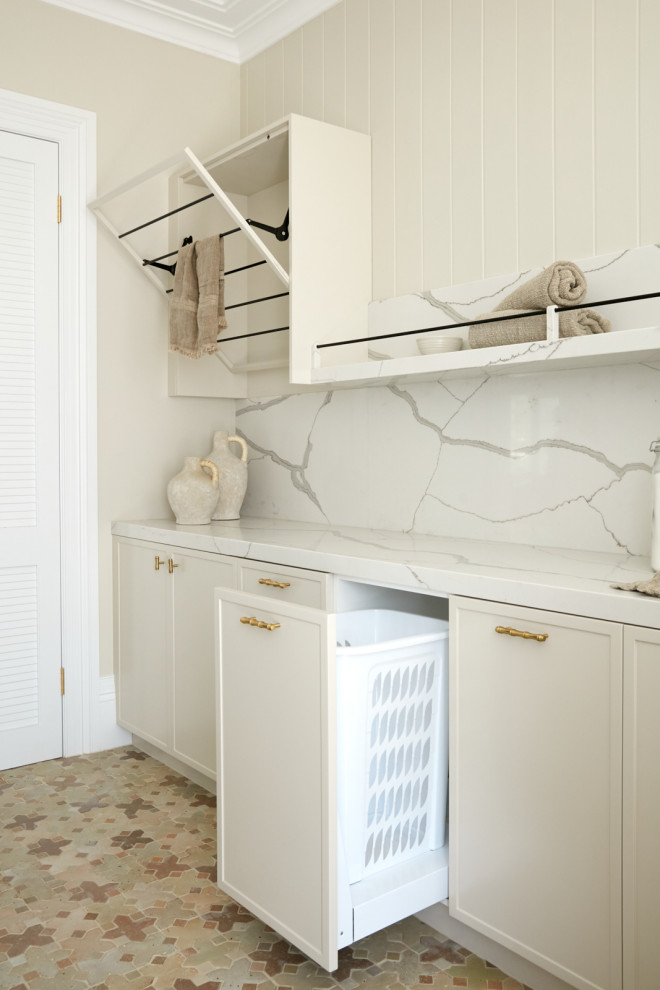 Rustik inredning av en stor vita vitt tvättstuga, med beige skåp, marmorbänkskiva, vitt stänkskydd, stänkskydd i marmor, beige väggar, klinkergolv i keramik, en tvättmaskin och torktumlare bredvid varandra och flerfärgat golv