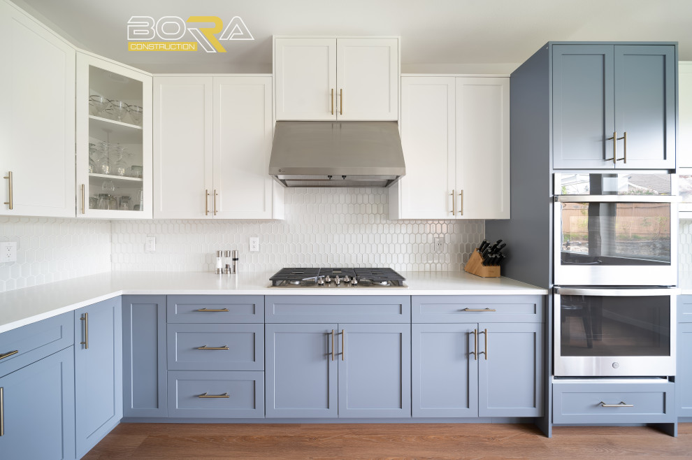 Example of a large transitional l-shaped medium tone wood floor and brown floor eat-in kitchen design in Seattle with an undermount sink, shaker cabinets, blue cabinets, quartz countertops, white backsplash, ceramic backsplash, stainless steel appliances, an island and white countertops
