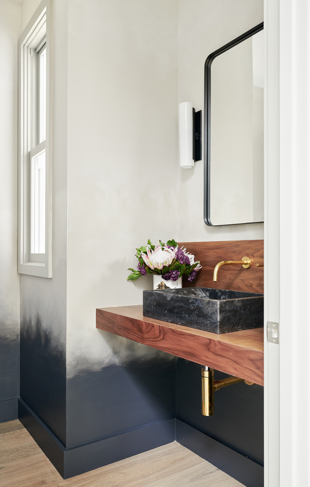 Design ideas for a large transitional powder room in San Francisco with medium wood cabinets, a wall-mount toilet, black tile, black walls, light hardwood floors, a vessel sink and wood benchtops.