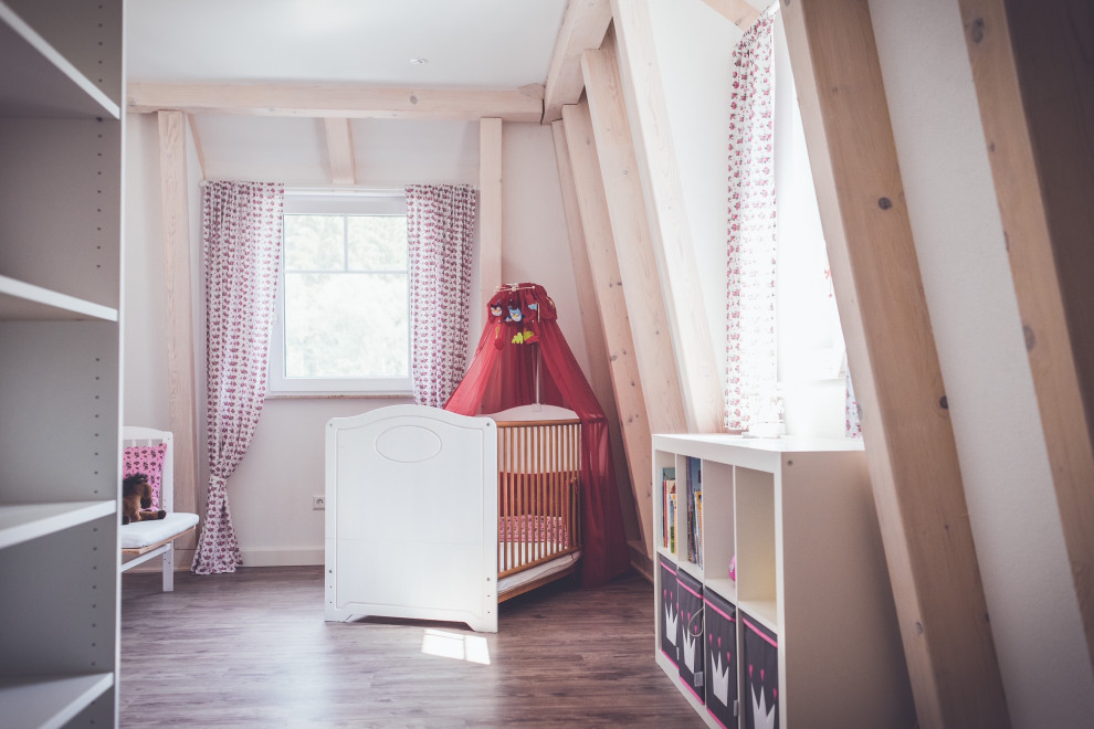 Immagine di una grande cameretta per neonata country con pareti bianche, parquet chiaro e travi a vista