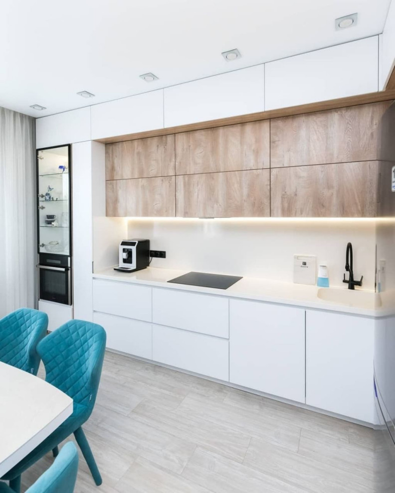 Large modern l-shaped open plan kitchen in Moscow with an integrated sink, flat-panel cabinets, white cabinets, solid surface benchtops, white splashback, glass sheet splashback, black appliances, laminate floors, no island, grey floor and white benchtop.