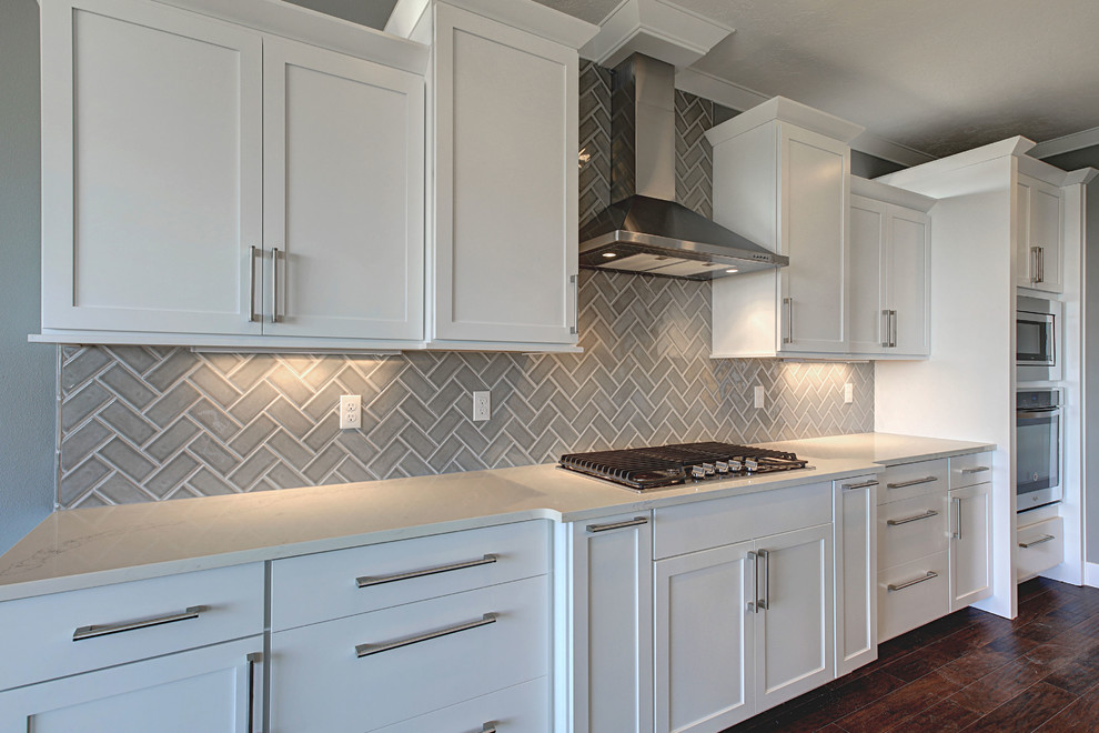 Example of a mid-sized transitional l-shaped medium tone wood floor open concept kitchen design in Seattle with an undermount sink, shaker cabinets, white cabinets, quartz countertops, gray backsplash, glass tile backsplash, stainless steel appliances and an island