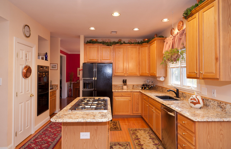 Mid-sized l-shaped medium tone wood floor kitchen pantry photo in DC Metro with a double-bowl sink, beaded inset cabinets, light wood cabinets, granite countertops, white backsplash, black appliances and an island