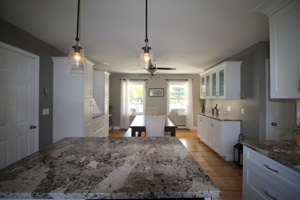 Example of a mid-sized transitional l-shaped light wood floor eat-in kitchen design in Burlington with a single-bowl sink, shaker cabinets, white cabinets, granite countertops, white backsplash, ceramic backsplash, stainless steel appliances and an island