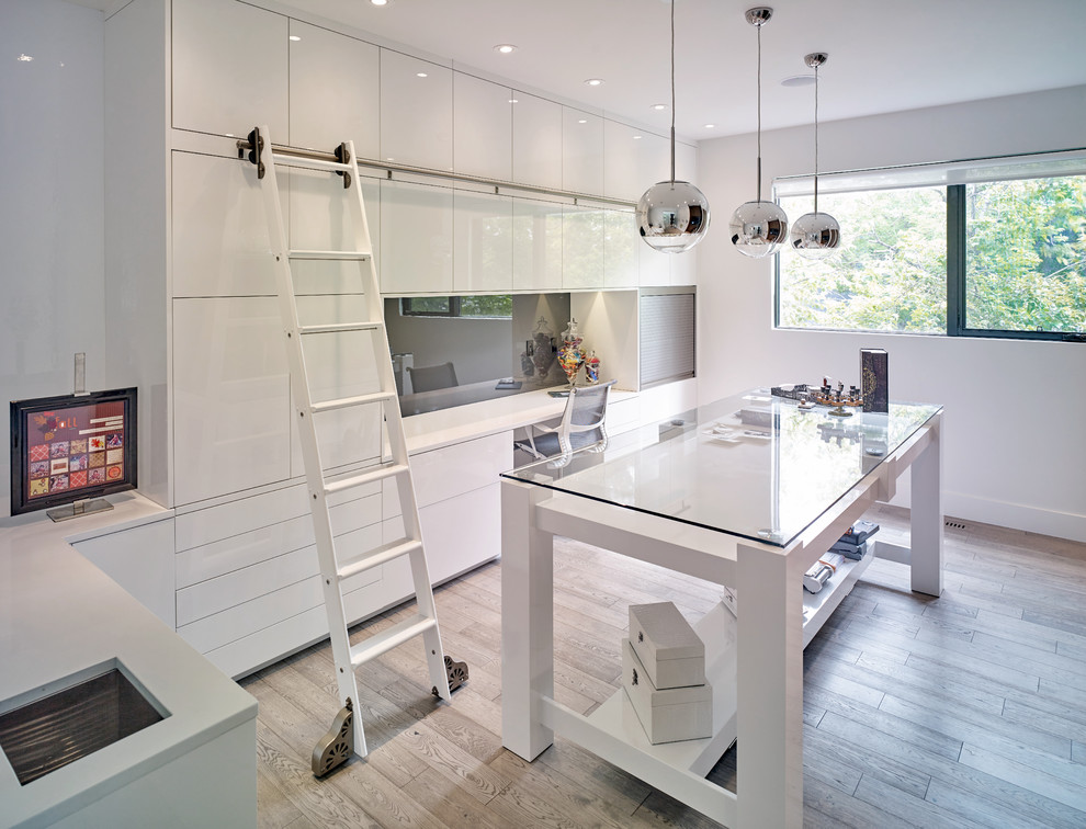 This is an example of a contemporary craft room in Calgary with white walls, light hardwood floors and a built-in desk.