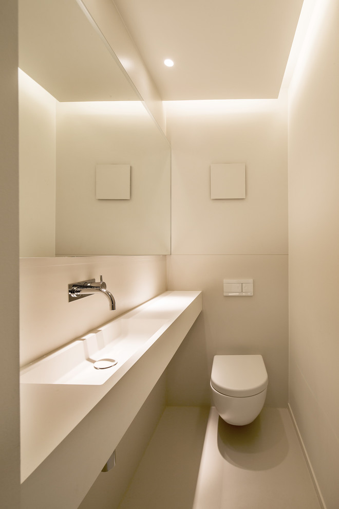 Inspiration for a small modern powder room in Stuttgart with a wall-mount toilet, white walls, an integrated sink and beige floor.