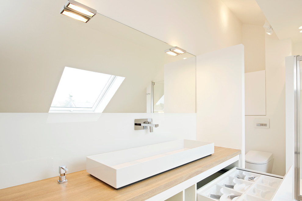 Photo of a mid-sized contemporary bathroom in Cologne with a trough sink, white cabinets, wood benchtops, a curbless shower, white walls, flat-panel cabinets, a wall-mount toilet and beige benchtops.
