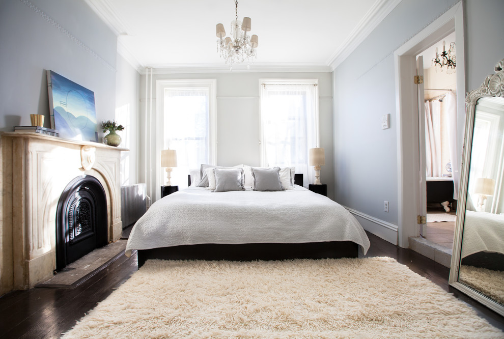 Transitional bedroom in New York with blue walls, dark hardwood floors and a standard fireplace.