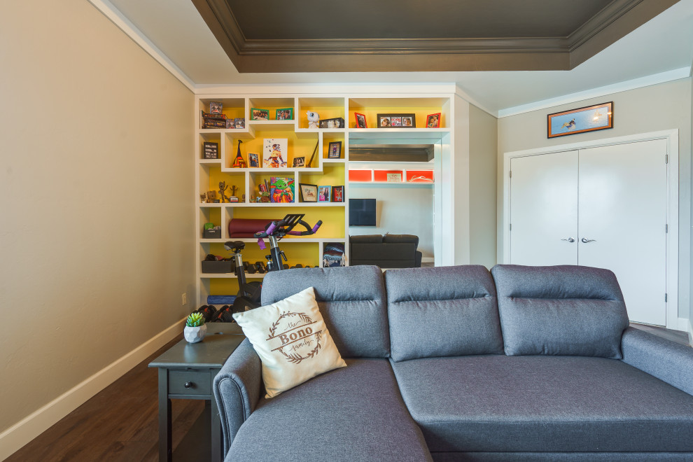 Cette photo montre une salle de séjour tendance de taille moyenne et fermée avec une bibliothèque ou un coin lecture, un mur jaune, un sol en bois brun, aucune cheminée, un téléviseur fixé au mur, un sol marron et un plafond voûté.