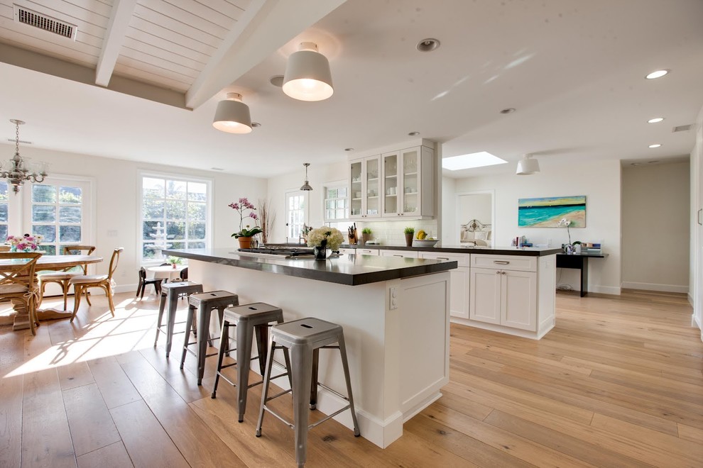 Mid-sized traditional l-shaped open plan kitchen in Orange County with glass-front cabinets, white cabinets, light hardwood floors, with island, brown floor and stainless steel appliances.