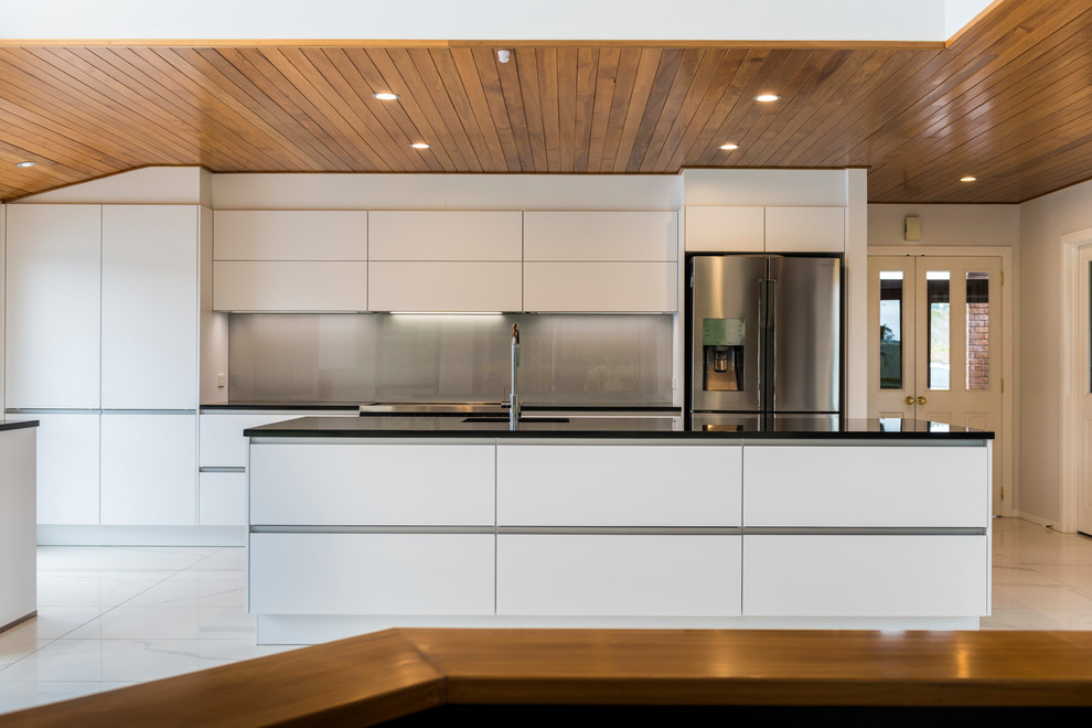 This is an example of a mid-sized contemporary galley kitchen pantry in Christchurch with an undermount sink, flat-panel cabinets, white cabinets, quartz benchtops, grey splashback, glass sheet splashback, stainless steel appliances, ceramic floors, with island and white floor.