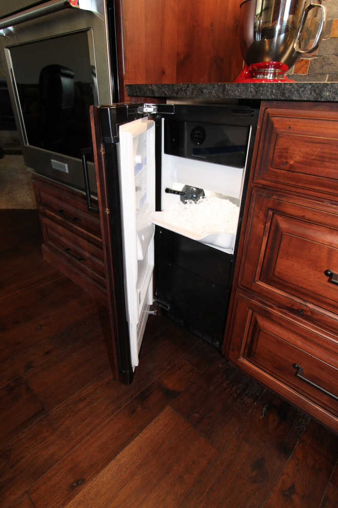Inspiration for a large rustic medium tone wood floor and brown floor kitchen remodel with raised-panel cabinets, medium tone wood cabinets, granite countertops, multicolored backsplash, stone tile backsplash, paneled appliances, an island and black countertops