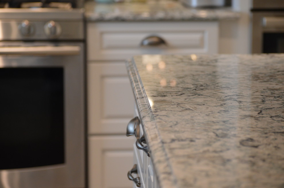 Home design - large transitional u-shaped ceramic tile and gray floor home design idea with a farmhouse sink, raised-panel cabinets, white cabinets, quartz countertops, gray backsplash, glass tile backsplash, stainless steel appliances and an island