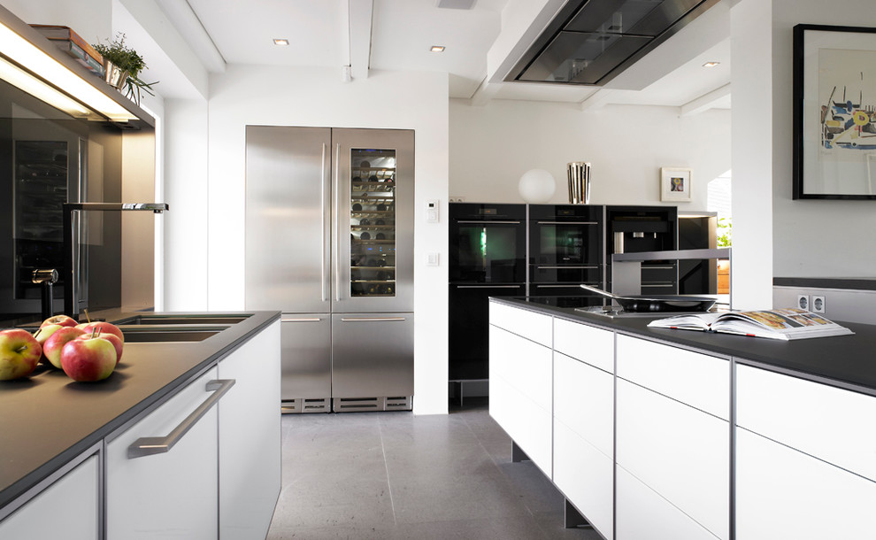 Inspiration for a large contemporary open plan kitchen in Other with a double-bowl sink, flat-panel cabinets, white cabinets, stainless steel appliances, concrete floors, black splashback and glass sheet splashback.