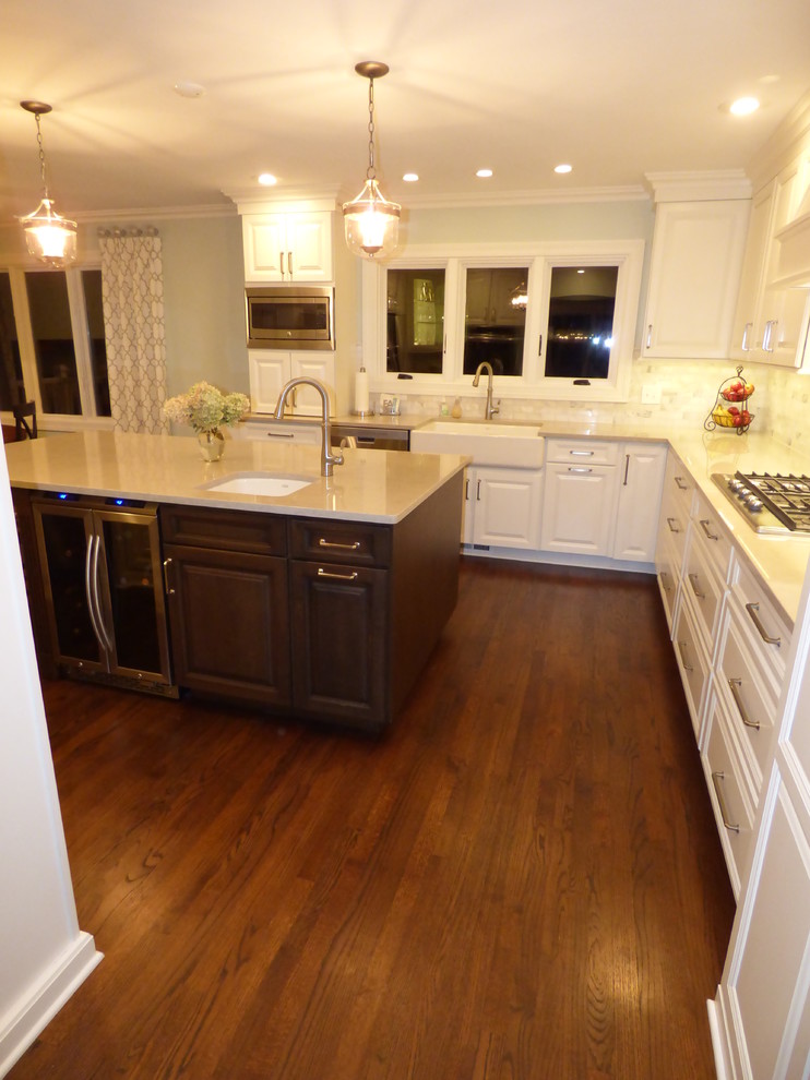Example of a large transitional u-shaped dark wood floor eat-in kitchen design in Chicago with a farmhouse sink, raised-panel cabinets, white cabinets, quartz countertops, gray backsplash, stone tile backsplash, stainless steel appliances and an island