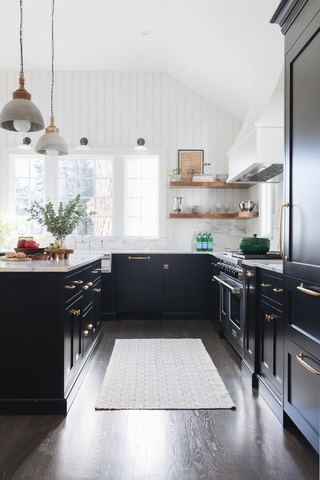 Inspiration for a mid-sized transitional l-shaped kitchen in Chicago with a farmhouse sink, shaker cabinets, black cabinets, marble benchtops, white splashback, marble splashback, panelled appliances, medium hardwood floors, with island and brown floor.