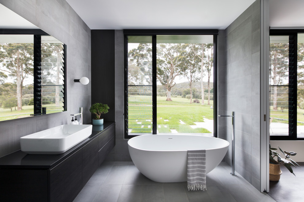 Photo of a modern master bathroom in Other with a freestanding tub, grey floor, flat-panel cabinets, black cabinets, gray tile, a vessel sink and black benchtops.