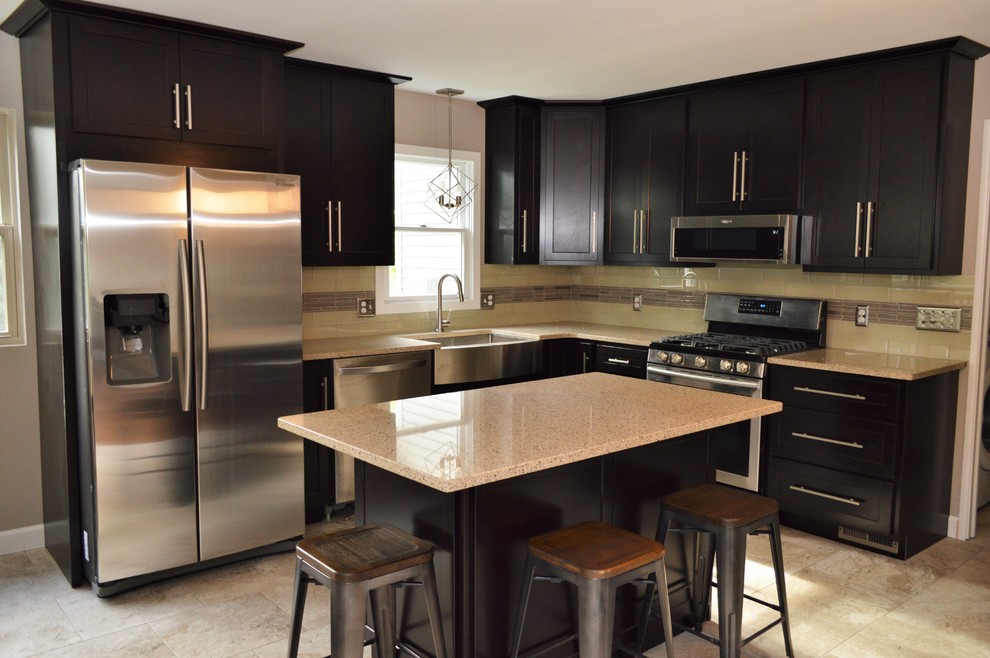 Photo of a mid-sized transitional l-shaped eat-in kitchen in Chicago with a farmhouse sink, shaker cabinets, black cabinets, quartzite benchtops, beige splashback, stainless steel appliances, ceramic floors, with island, beige floor and beige benchtop.