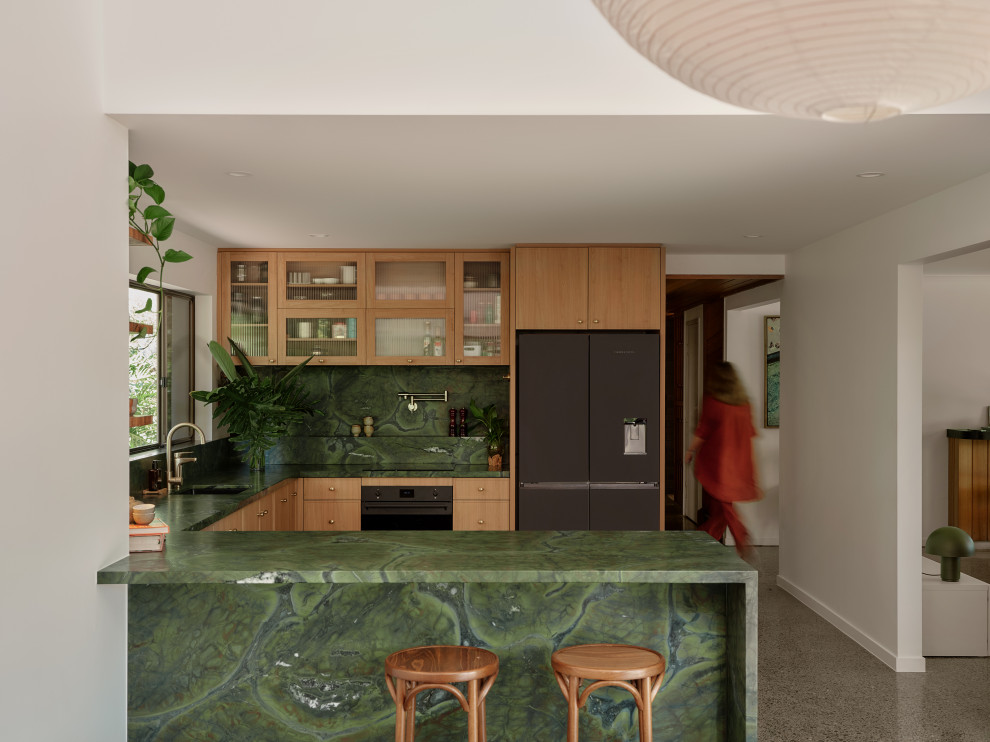 Photo of a contemporary u-shaped kitchen in Brisbane with an undermount sink, flat-panel cabinets, medium wood cabinets, green splashback, stone slab splashback, black appliances, a peninsula, grey floor and green benchtop.