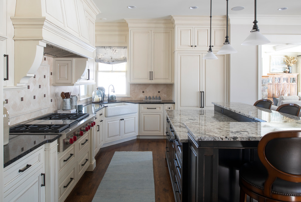 Traditional l-shaped kitchen in Minneapolis with a farmhouse sink, raised-panel cabinets, beige cabinets, beige splashback, stainless steel appliances, dark hardwood floors, with island, brown floor and grey benchtop.