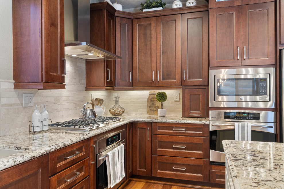 Mid-sized transitional l-shaped medium tone wood floor and brown floor open concept kitchen photo in San Francisco with an undermount sink, recessed-panel cabinets, dark wood cabinets, granite countertops, beige backsplash, marble backsplash, stainless steel appliances, an island and beige countertops
