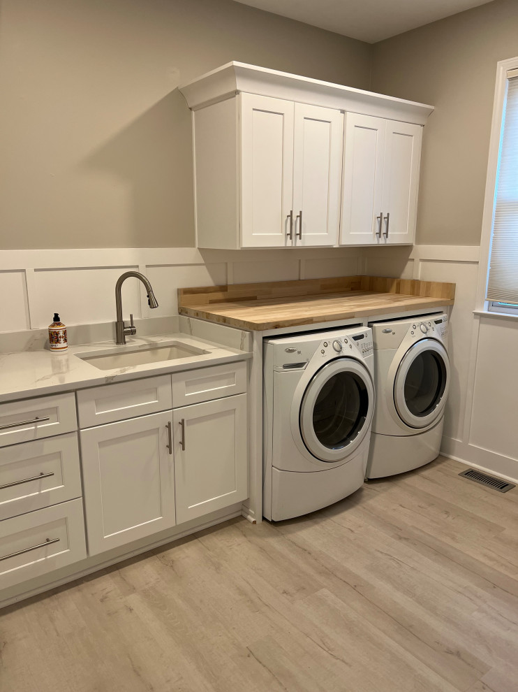 Inspiration for a large transitional single-wall utility room in Atlanta with a single-bowl sink, shaker cabinets, white cabinets, wood benchtops, white splashback, timber splashback, grey walls, vinyl floors, a side-by-side washer and dryer, grey floor, brown benchtop and wood walls.