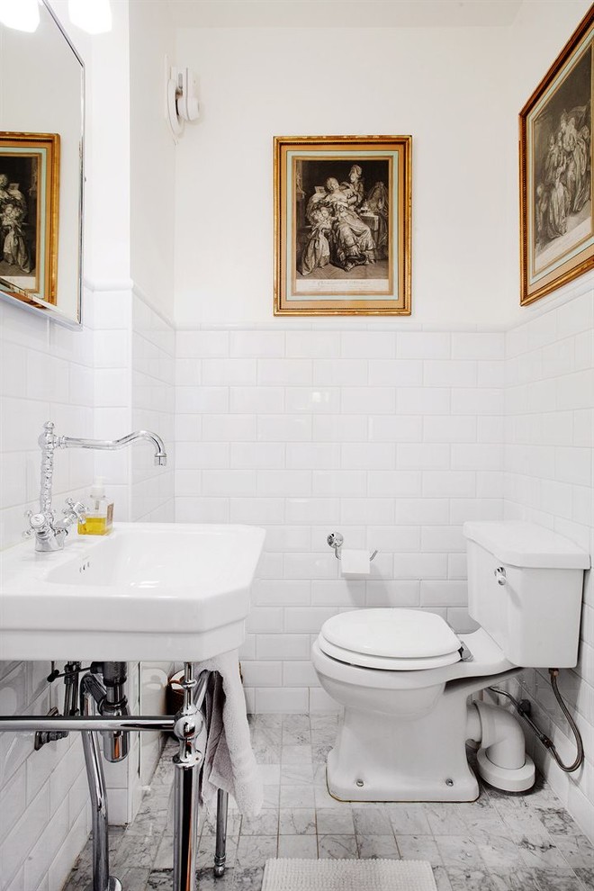 Inspiration for a mid-sized traditional powder room in Stockholm with a two-piece toilet, white tile, subway tile, white walls, marble floors, a console sink and grey floor.