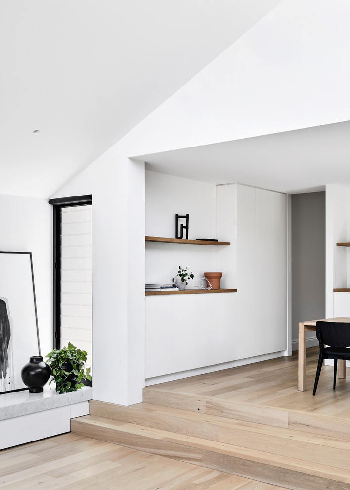Photo of a mid-sized contemporary kitchen/dining combo in Melbourne with white walls, light hardwood floors, a standard fireplace, a metal fireplace surround and brown floor.