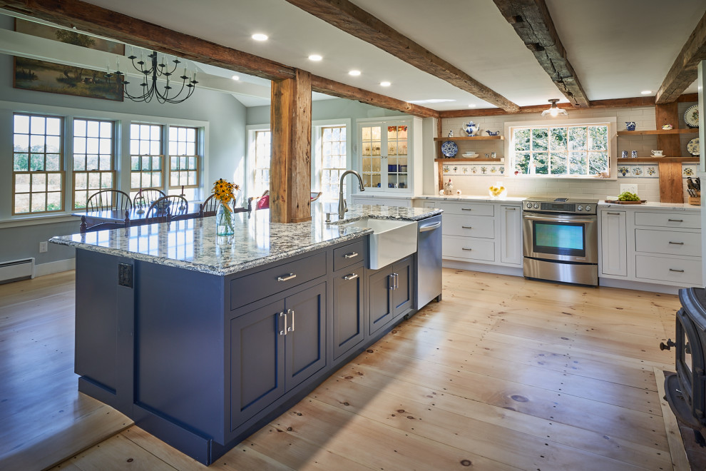 Lantlig inredning av ett blå blått kök och matrum, med en rustik diskho, skåp i shakerstil, vita skåp, bänkskiva i kvarts, vitt stänkskydd, stänkskydd i tunnelbanekakel, rostfria vitvaror, ljust trägolv, en köksö och brunt golv