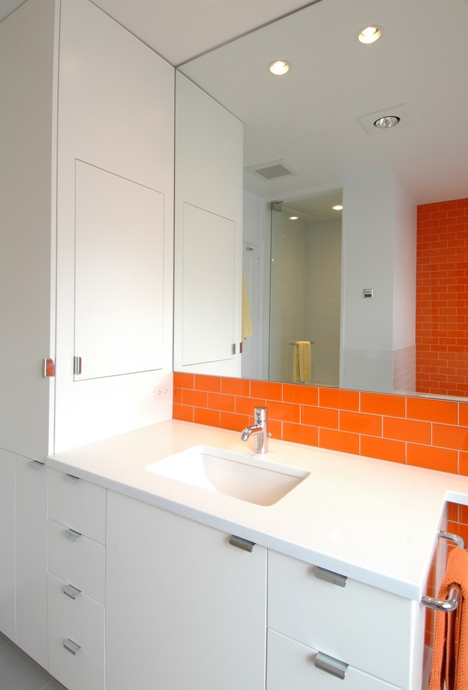 This is an example of a contemporary bathroom in New York with an undermount sink, flat-panel cabinets, white cabinets, solid surface benchtops, orange tile and subway tile.