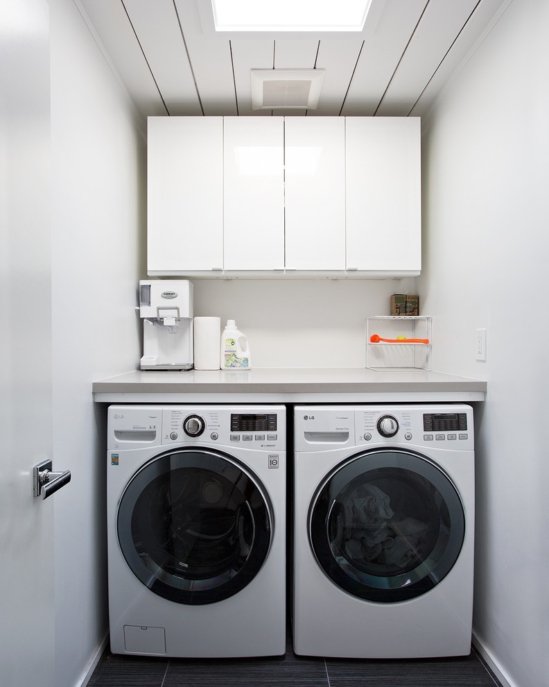 This is an example of a small midcentury single-wall dedicated laundry room in San Francisco with flat-panel cabinets, white cabinets, white walls, a side-by-side washer and dryer, black floor and grey benchtop.