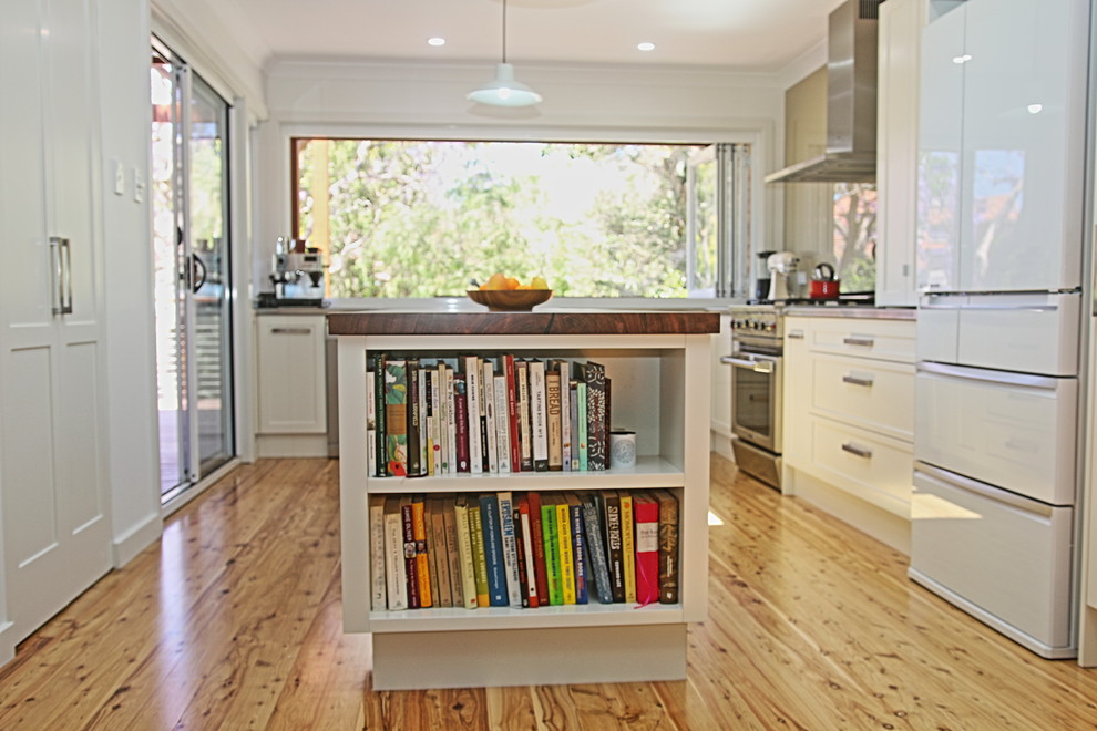 Design ideas for a mid-sized transitional l-shaped kitchen pantry in Sydney with a double-bowl sink, shaker cabinets, white cabinets, stainless steel benchtops, black splashback, glass sheet splashback, stainless steel appliances, light hardwood floors and with island.
