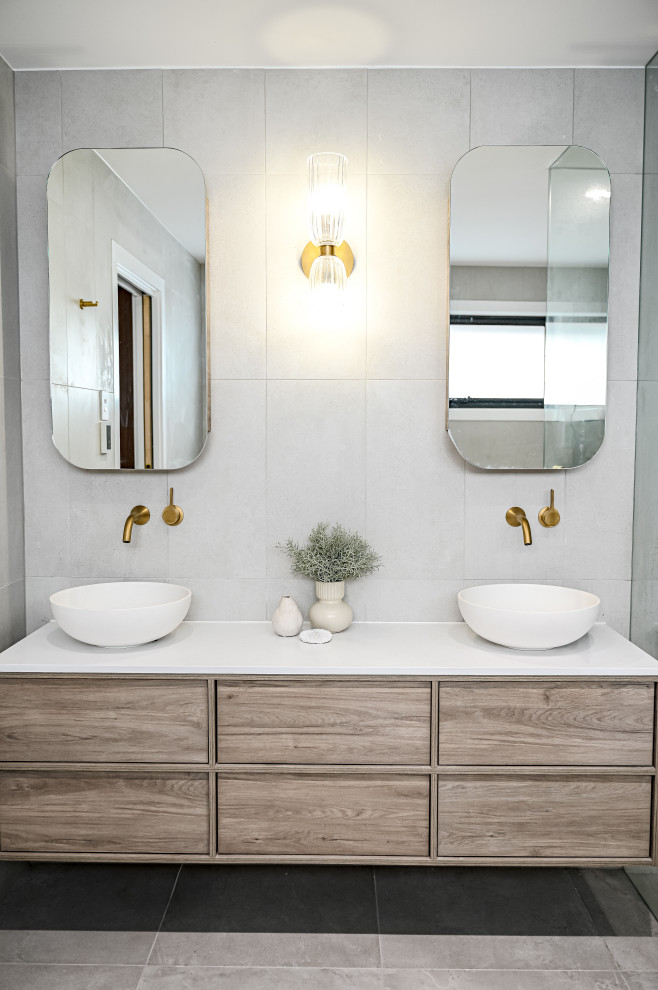 This is an example of a large contemporary master bathroom in Sydney with shaker cabinets, light wood cabinets, a freestanding tub, a corner shower, a one-piece toilet, gray tile, stone tile, grey walls, marble floors, a trough sink, solid surface benchtops, grey floor, a hinged shower door, white benchtops, a double vanity and a floating vanity.