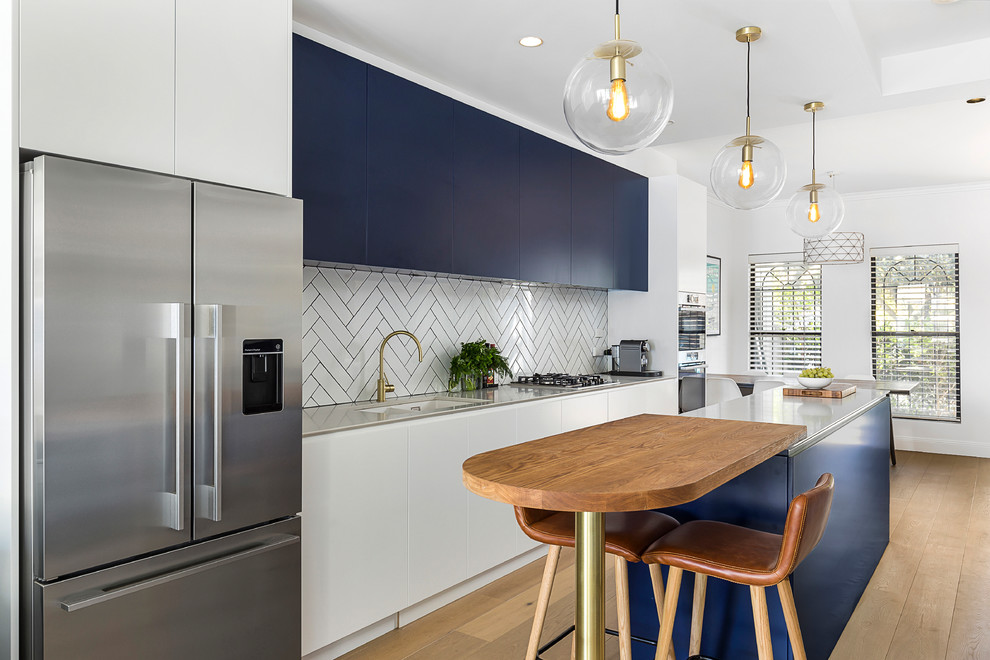 Photo of a large contemporary galley open plan kitchen in Sydney with an undermount sink, flat-panel cabinets, blue cabinets, quartz benchtops, white splashback, subway tile splashback, stainless steel appliances, light hardwood floors, with island, brown floor and white benchtop.