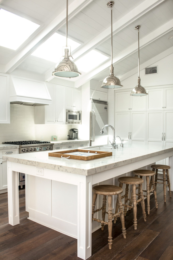 Photo of a mid-sized beach style galley open plan kitchen in Los Angeles with an undermount sink, shaker cabinets, white cabinets, quartzite benchtops, white splashback, with island, brown floor, stainless steel appliances and medium hardwood floors.
