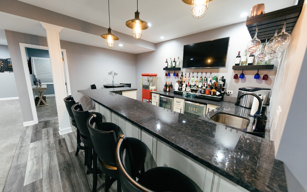 Inspiration for a mid-sized transitional u-shaped seated home bar in Chicago with an undermount sink, raised-panel cabinets, white cabinets, quartzite benchtops, laminate floors, grey floor and black benchtop.