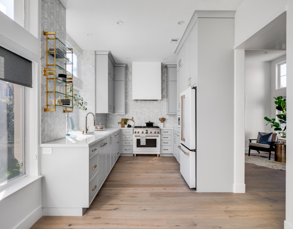 Photo of a small contemporary u-shaped separate kitchen in Los Angeles with an undermount sink, shaker cabinets, grey cabinets, quartz benchtops, white splashback, marble splashback, white appliances, medium hardwood floors, no island, brown floor and white benchtop.