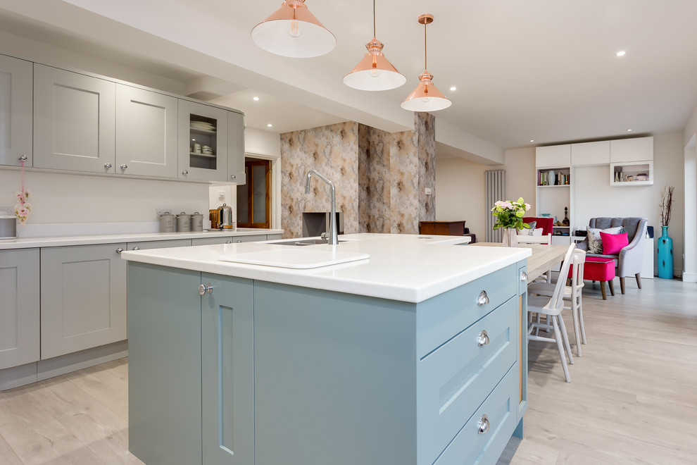 This is an example of a medium sized eclectic l-shaped kitchen/diner in Hampshire with a submerged sink, shaker cabinets, grey cabinets, composite countertops, grey splashback, stainless steel appliances, laminate floors, an island, beige floors and white worktops.